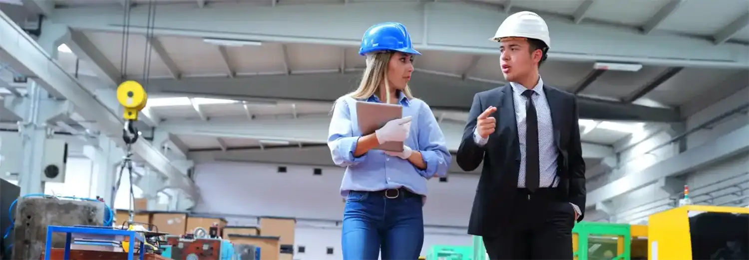 Directeur industriel de transition en visite d’usine, échangeant avec une collaboratrice sur le terrain pour superviser la production et piloter la performance industrielle.
