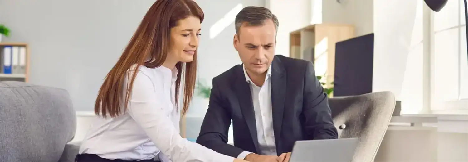 Directeur marketing et communication de transition travaillant en collaboration avec une collègue, analysant des données sur ordinateur pour piloter la stratégie et accompagner la transformation de l’entreprise.